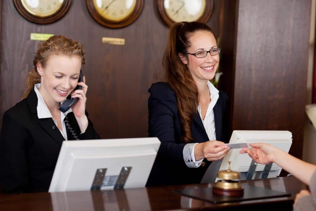 Two Female Employees At Hotel Reception Desk Small